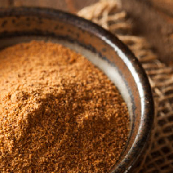 Ground cinnamon in a dark ceramic bowl on burlap fabric