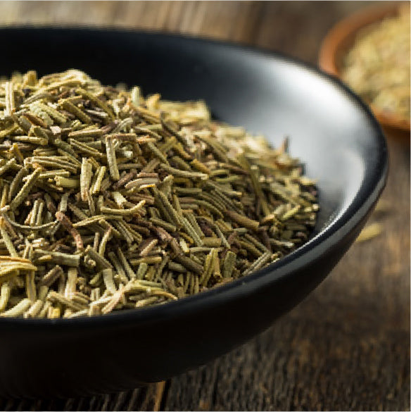 Dried rosemary piled in a black bowl on a wooden surface.