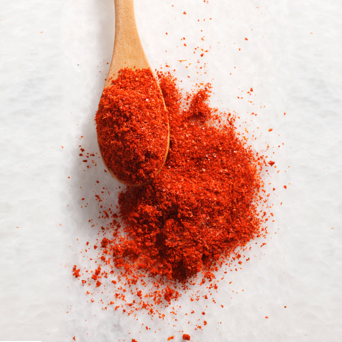 Wooden spoon heaped with red chili powder beside a red chili on a white background
