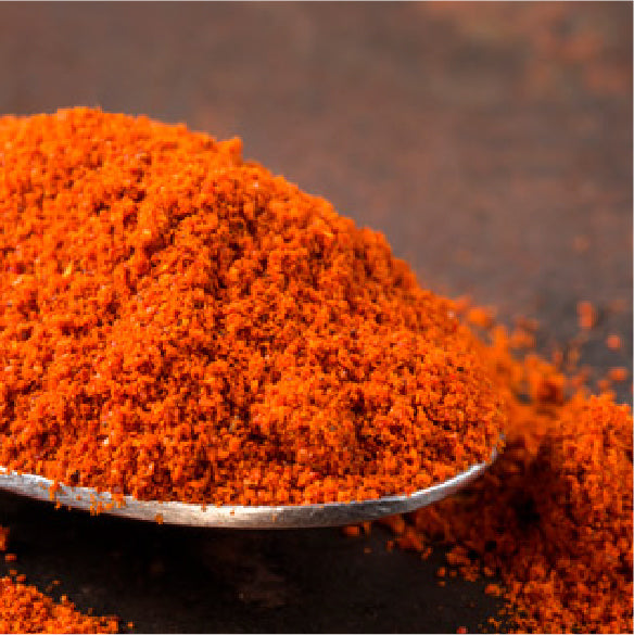 Pile of bright orange paprika powder resting on a metal spoon.