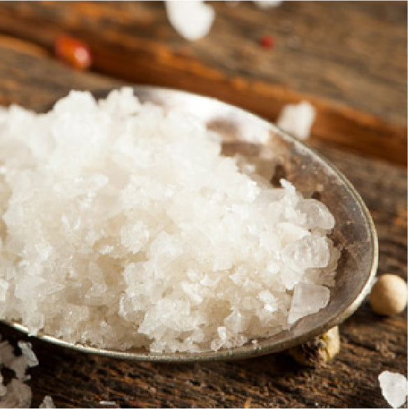 Coarse sea salt in a metal spoon on a rustic wooden surface